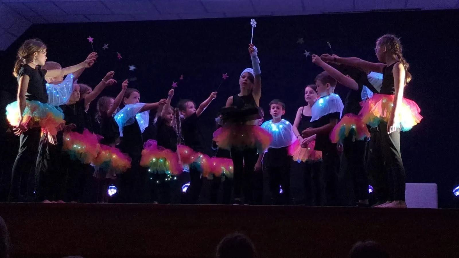 Les enfants des ateliers sur scène, tutus lumineux et baguettes étoilées, spectacle « Dans les étoiles », mai 2025