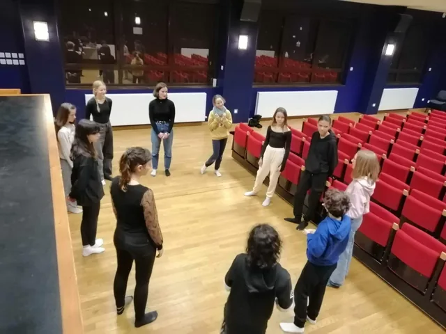 Atelier adolescents en cercle sur le parquet, fauteuils rouges de la salle